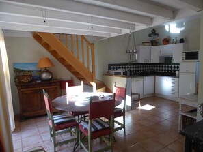A dining area with a wooden staircase, a kitchen with white cabinets, and a tiled floor. - Le Gîte Saint Martin – ROQUEFORT DES CORBIERES (ROQUEFORT DES CORBIERES)