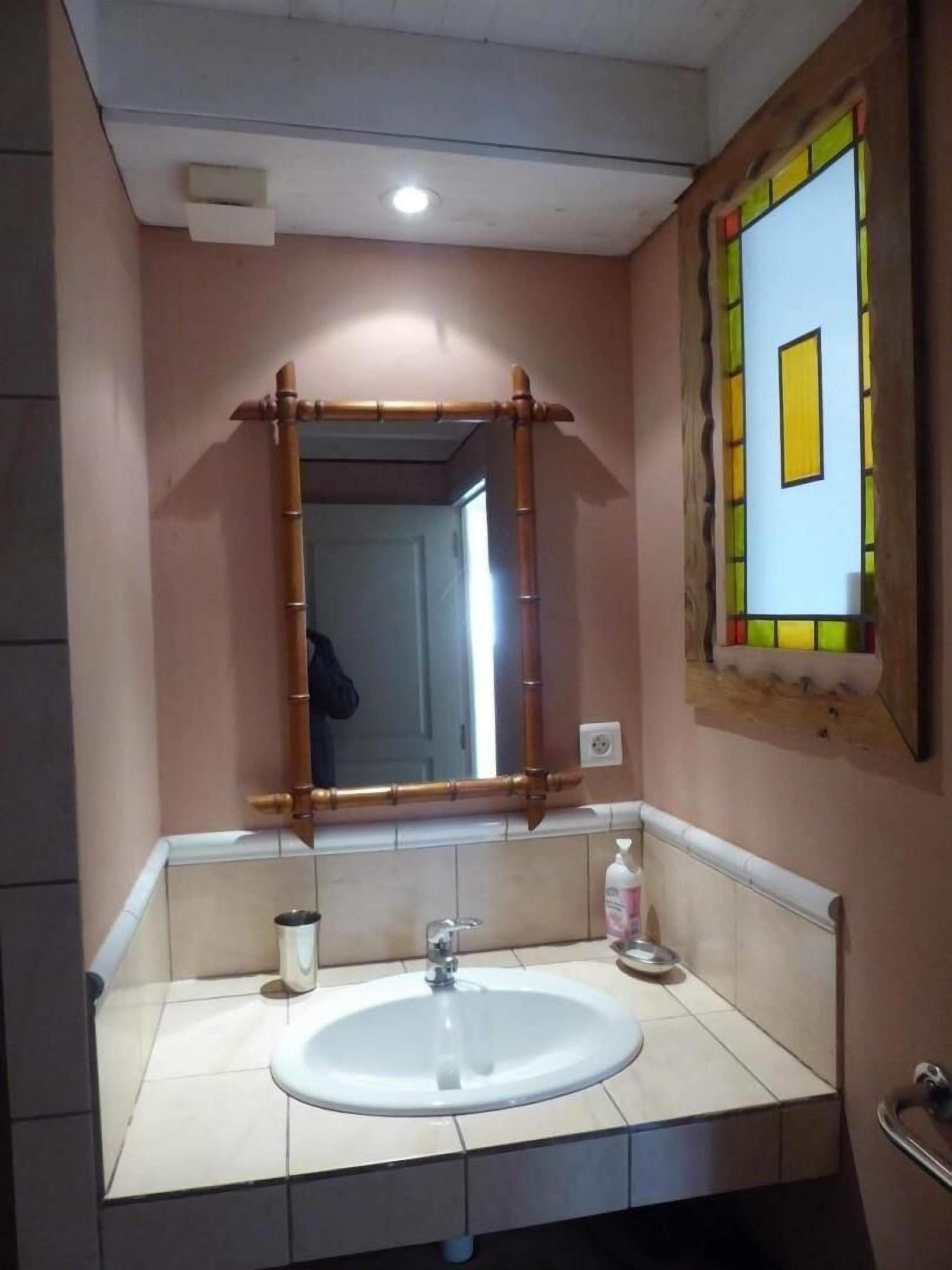 A bathroom with a white sink, a mirror, and a window with a stained glass design.