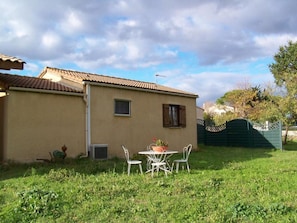 Uma casa com telhado de telhas, uma janela pequena e um pátio com mesa e cadeiras.