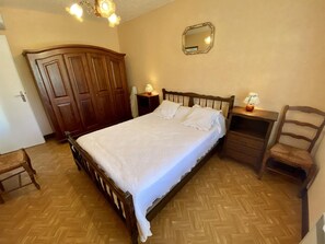 Ein Schlafzimmer mit einem Holzbett, einem Nachttisch, einem Sessel, einem Kleiderschrank und einem Spiegel an der Wand.