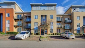Eine Reihe moderner Apartmenthäuser mit Balkonen, ein kleiner Baum davor und zwei parkende Autos.