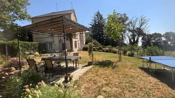 Un espacio exterior residencial con un porche cubierto, una mesa con sillas, una mesa de ping pong y una piscina.