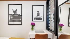Ein Hotelzimmer mit weißem Schreibtisch, zwei Stühlen, einem Bett mit gelber Decke und zwei gerahmten Bildern an der Wand.