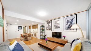 Ein modernes Wohnzimmer mit Sofa, Couchtisch und Fernseher. Es gibt einen Essbereich mit Stühlen und einem Tisch. An den Wänden hängen gerahmte Bilder.