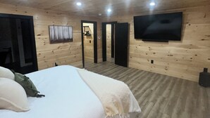 Un dormitorio con una cama, un televisor montado en la pared y un techo de madera.