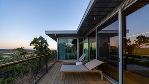 Un balcon moderne avec une terrasse en bois, des portes vitrées et un fauteuil de relaxation.