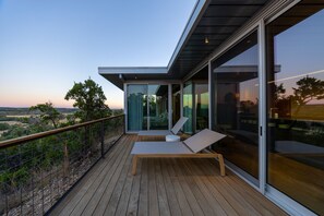 Ein moderner Balkon mit Holzboden, Glastüren und einer Liege.