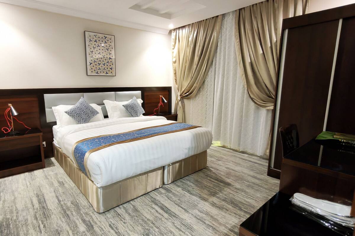A hotel room with a large bed, a nightstand, a desk, a TV, and a wardrobe.