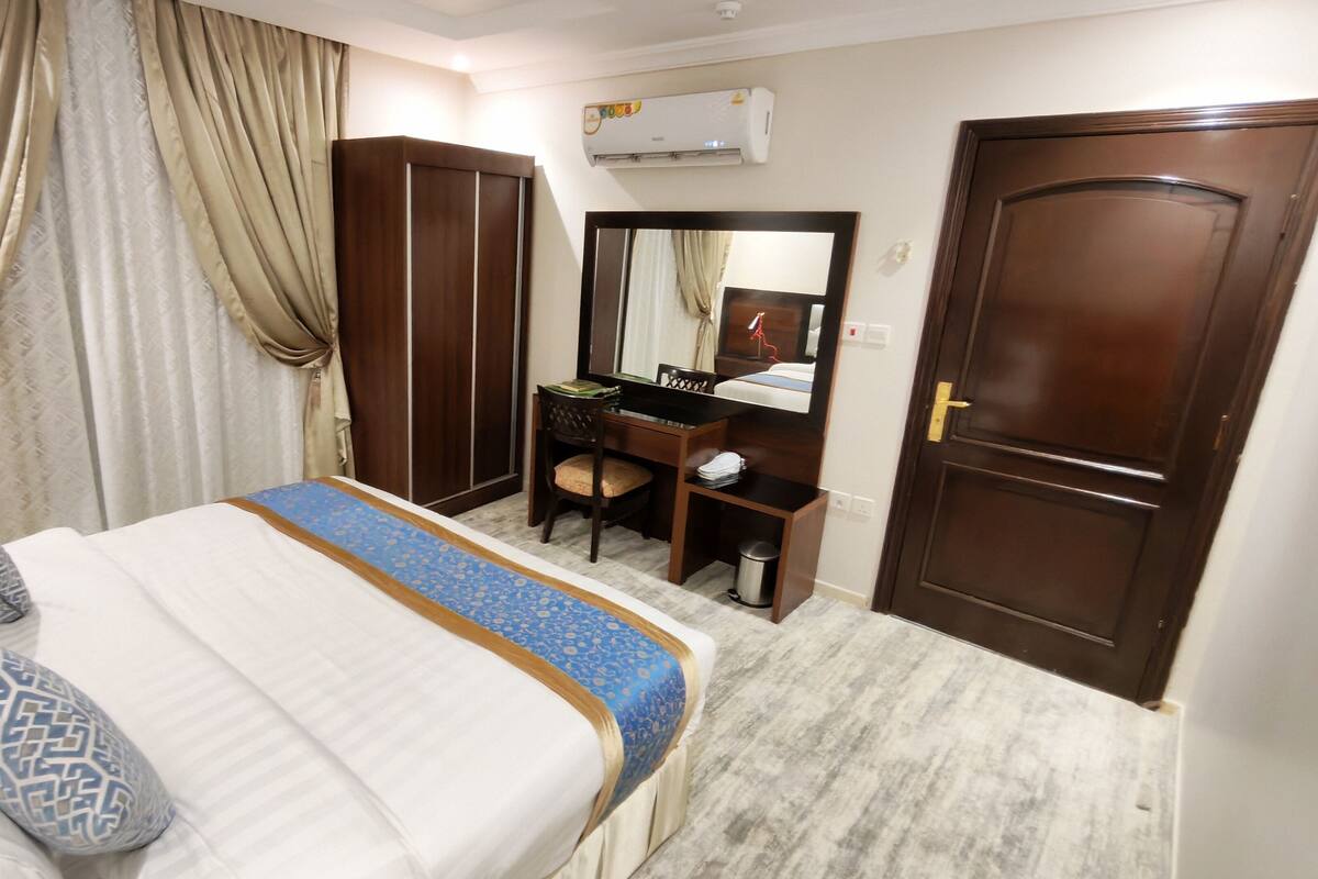 A hotel room with a bed, a desk, a chair, a wardrobe, and a mirror.