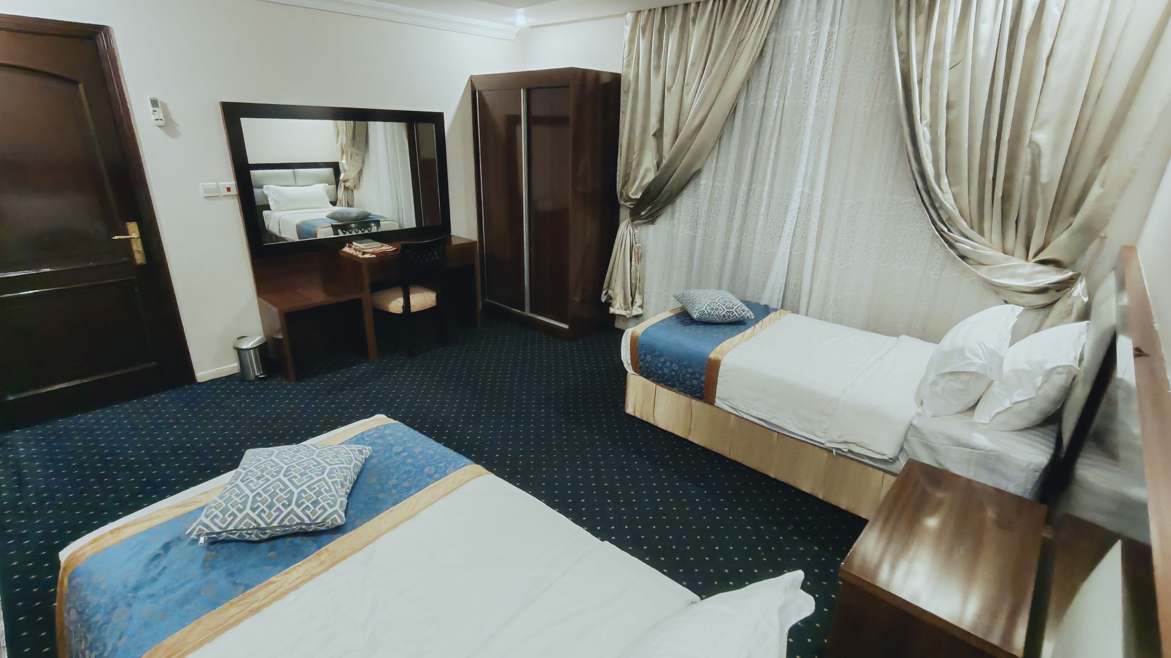 A hotel room with a bed, a desk, a wardrobe, and a mirror.