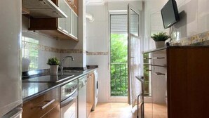 Ett modernt kök med rostfria vitvaror, träskåp och ett stort fönster med utsikt över grönområden.