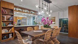 A modern kitchen with a dining area, wooden shelves, wicker chairs, and a central island with a vase of flowers. - Luxurious Artistic Compound as seen on TV (Los Angeles)