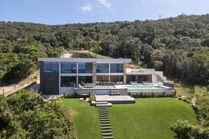 A modern house with a large glass facade, a swimming pool, and a well-maintained lawn. - Villa DEA - 6 bedrooms, panoramic sea view, front of beach, swimming pool (COTI CHIAVARI)