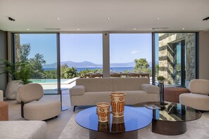 A modern living room with a sofa, armchairs, a glass coffee table, and large windows offering a view of a pool and mountains. - Villa DEA - 6 bedrooms, panoramic sea view, front of beach, swimming pool (COTI CHIAVARI)