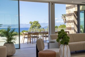 Una sala de estar moderna con ventanas amplias, un sofá, una mesa de comedor con sillas y plantas en macetas.