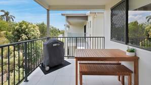Ein Balkon mit Grill, Holztisch und einer Topfpflanze.