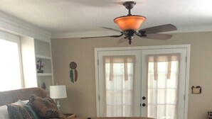 Ein Schlafzimmer mit einem großen Bett, einem Deckenventilator, einem Fenster und einer mit Vorhängen versehenen Tür.