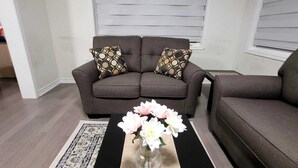 Un salon avec un canapé gris, des coussins à motifs, une table basse noire ornée d’un vase de fleurs et un tapis à motifs.