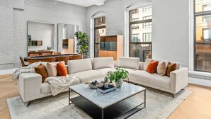 A modern living room with a sectional sofa, a coffee table, and a dining area with a wooden table and chairs. - NEW Luxe Downtown Waterfront with Game Room | FREE Parking Walkable to Quincy Mkt (Boston)