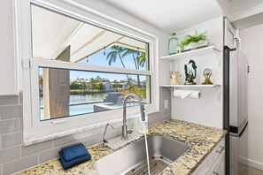 A kitchen with a large window, granite countertop, stainless steel sink, and a refrigerator. - Waterfront 3BR w/ Heated Pool, Hot Tub, Dock & Game Room (Largo)