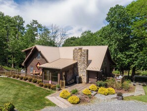 A log cabin with a stone chimney, a deck, and a well-maintained garden. - Blowing Rock Haven-Pet Friendly, Short Drive to Skiing (Blowing Rock)