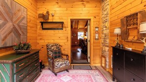 Ein Blockhaus-Interieur mit einer Holzwand, einem gemusterten Sessel, einer Kommode und einer Steinsäule.