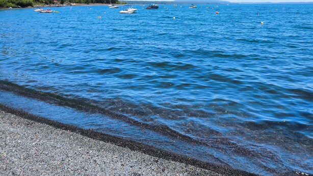 A beach with boats on the water and a rocky shoreline. - Bordelago Pucón Playa Privada (Araucanía)
