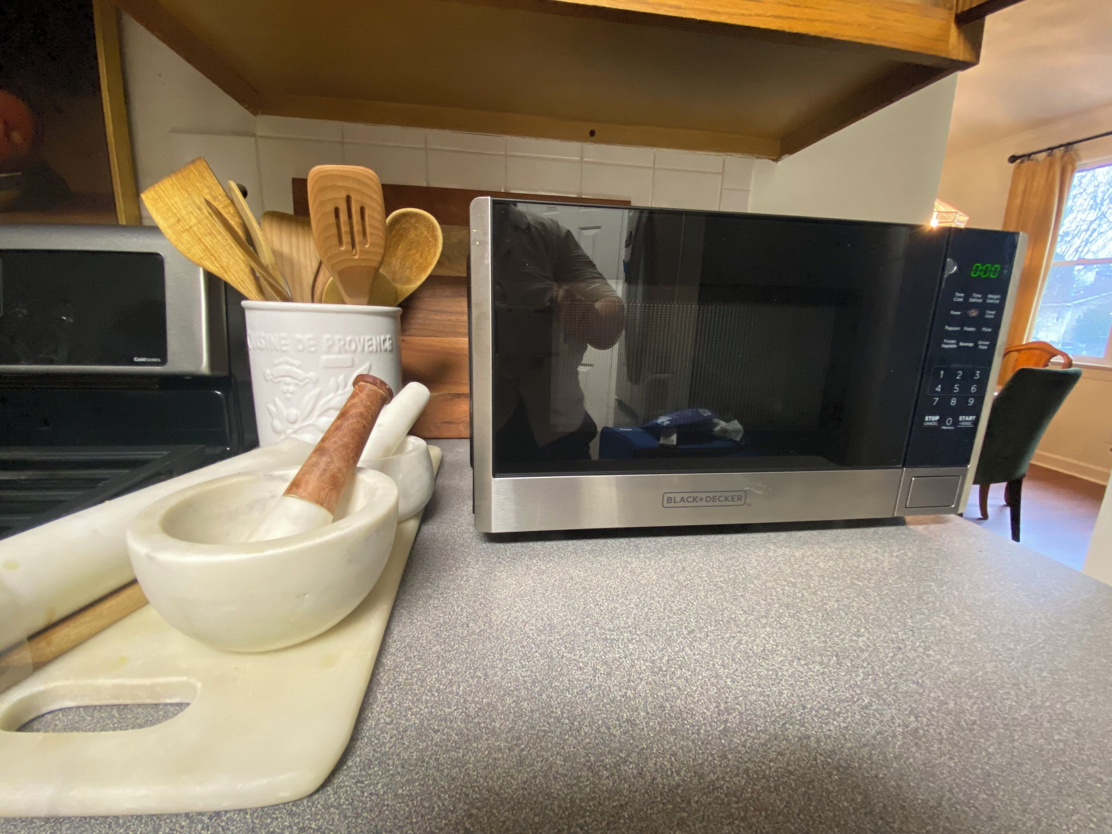 Une cuisine équipée d’un four à micro-ondes, d’une planche à découper en bois, d’un mortier et d’un pilon, ainsi que d’un ensemble d’ustensiles de cuisine en bois.