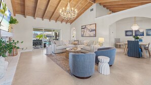 A spacious living area with a high wooden ceiling, a chandelier, a sectional sofa, and a dining area with a table and chairs. - Waterfront Lux 4BR! New Reno with Heated Pool + Outdoor Kitchen (Lighthouse Point)