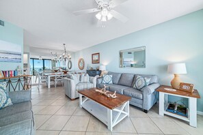 A spacious living room with a dining area, a grey sofa, a wooden coffee table, and a ceiling fan. - Summer House 405B | Pools, Hot Tub, Tennis | My Beach Getaways (Orange Beach)