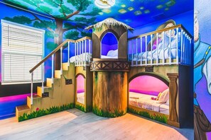 Ein Spielzimmer mit Rutsche, Kletterwand und einer Wandmalerei mit Waldszene.