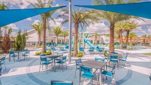 Un espace aménagé au bord de la piscine, avec des chaises et des tables bleues, des palmiers et un toboggan aquatique.