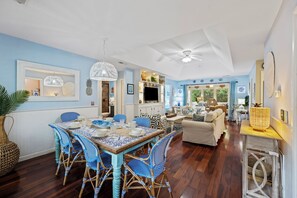 A spacious living area with a dining table, blue patterned chairs, and a ceiling fan. - 3 BD Sparrow Pond Cottage, Close to Beach, Community Pool, Privacy! Fun Decor! (Kiawah Island)