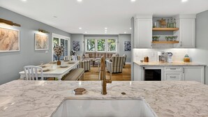 A modern kitchen with marble countertops, a central island, and a dining area with a sofa and chairs. - Unbeatable, OCEANFRONT Views - 4 bedroom Pelican Watch, FULLY RENOVATED! (Seabrook Island)