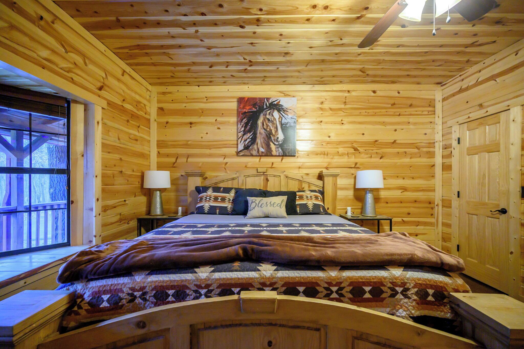 Une chambre à coucher dans un chalet en bois, avec un lit, deux lampes de chevet, un tableau et une fenêtre.