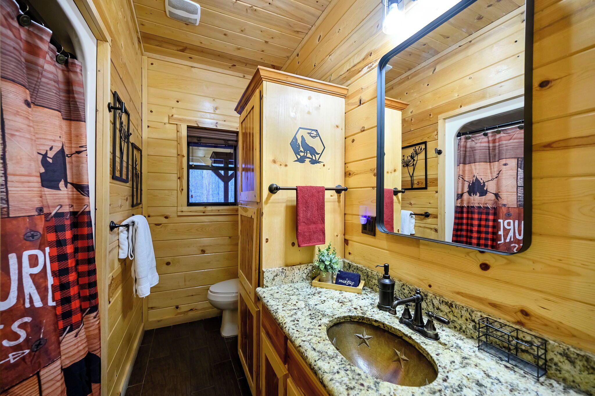 Une salle de bain rustique, avec des murs en bois, un comptoir en granit, un lavabo, des toilettes et un miroir.