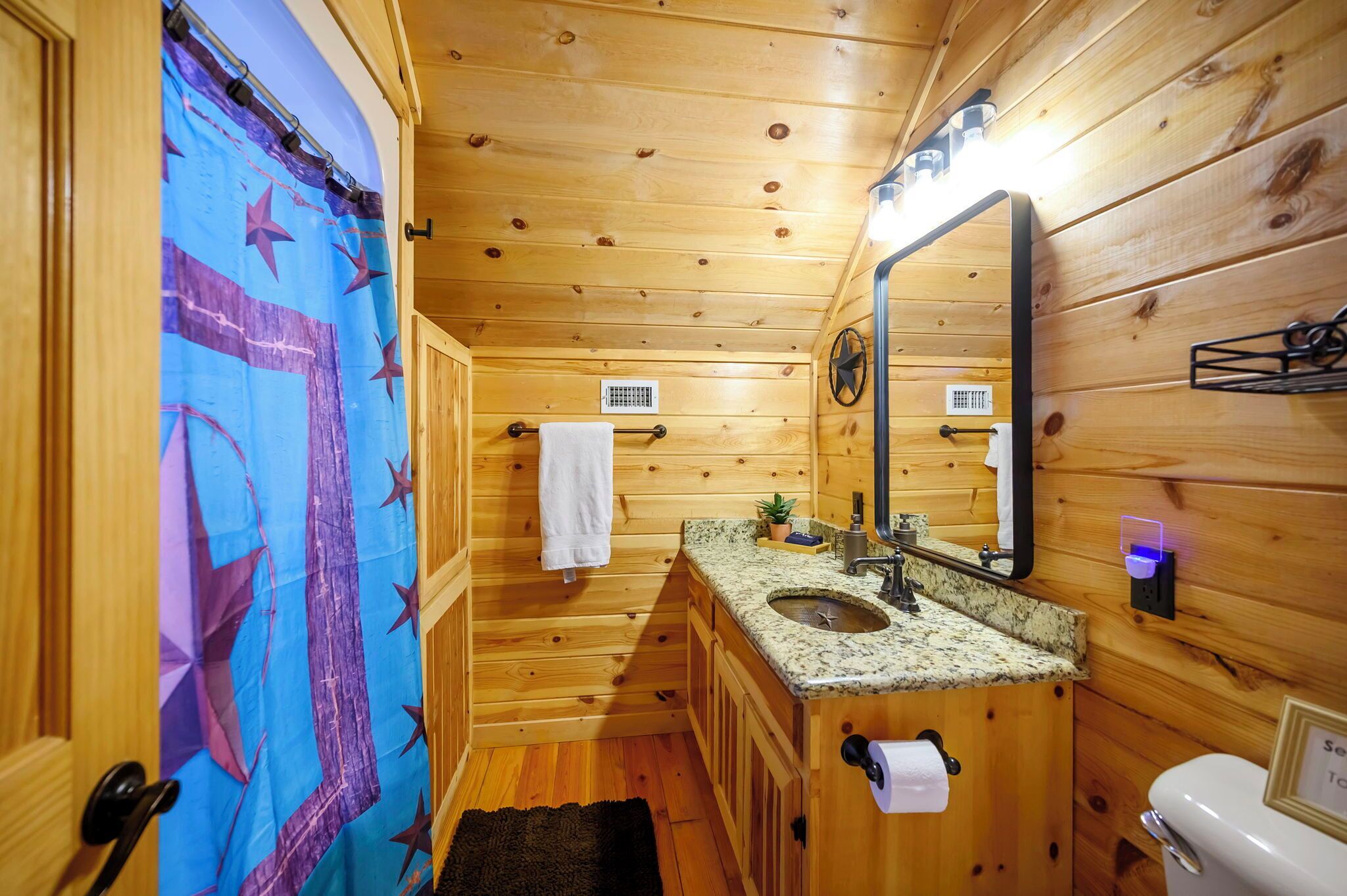 Une salle de bain rustique, aménagée dans une cabane en bois, comprenant un lavabo, un miroir, un porte-serviettes et des toilettes.