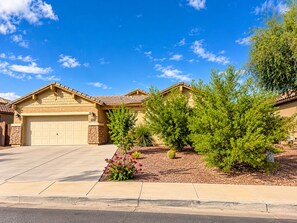 A residential house with a garage, a driveway, and a well-maintained lawn with various shrubs and a small garden. - Perfect 1-level, 4-bedroom, 2100 sqft house with AC in charming Avondale, AZ (Avondale)