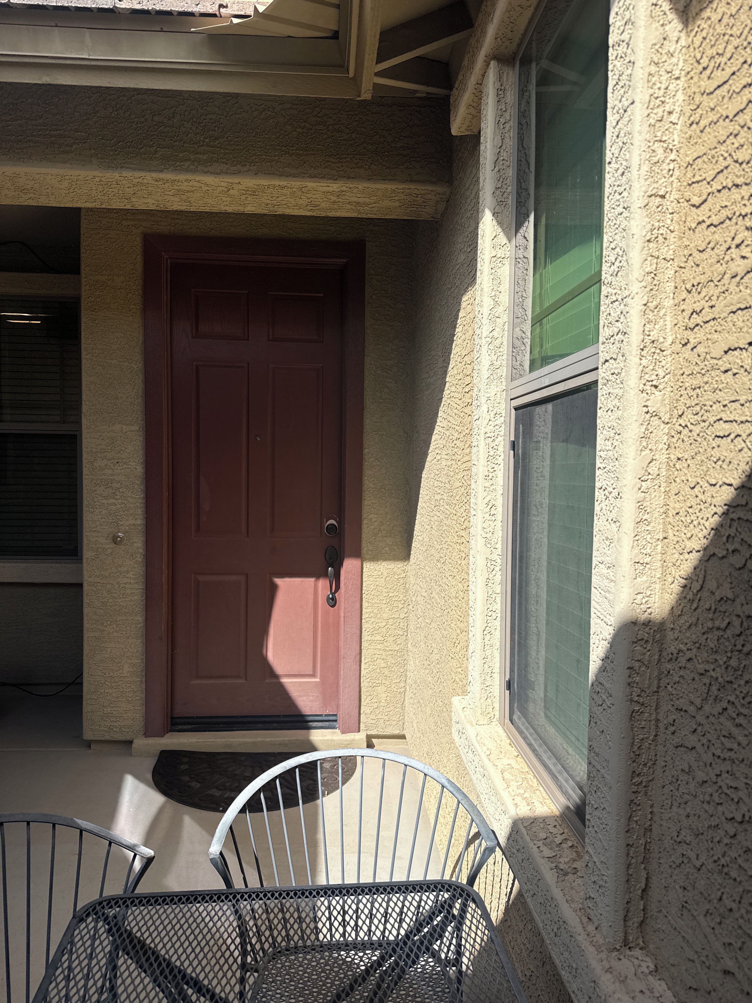 A house with a red door, a window with green blinds, and a metal chair outside.