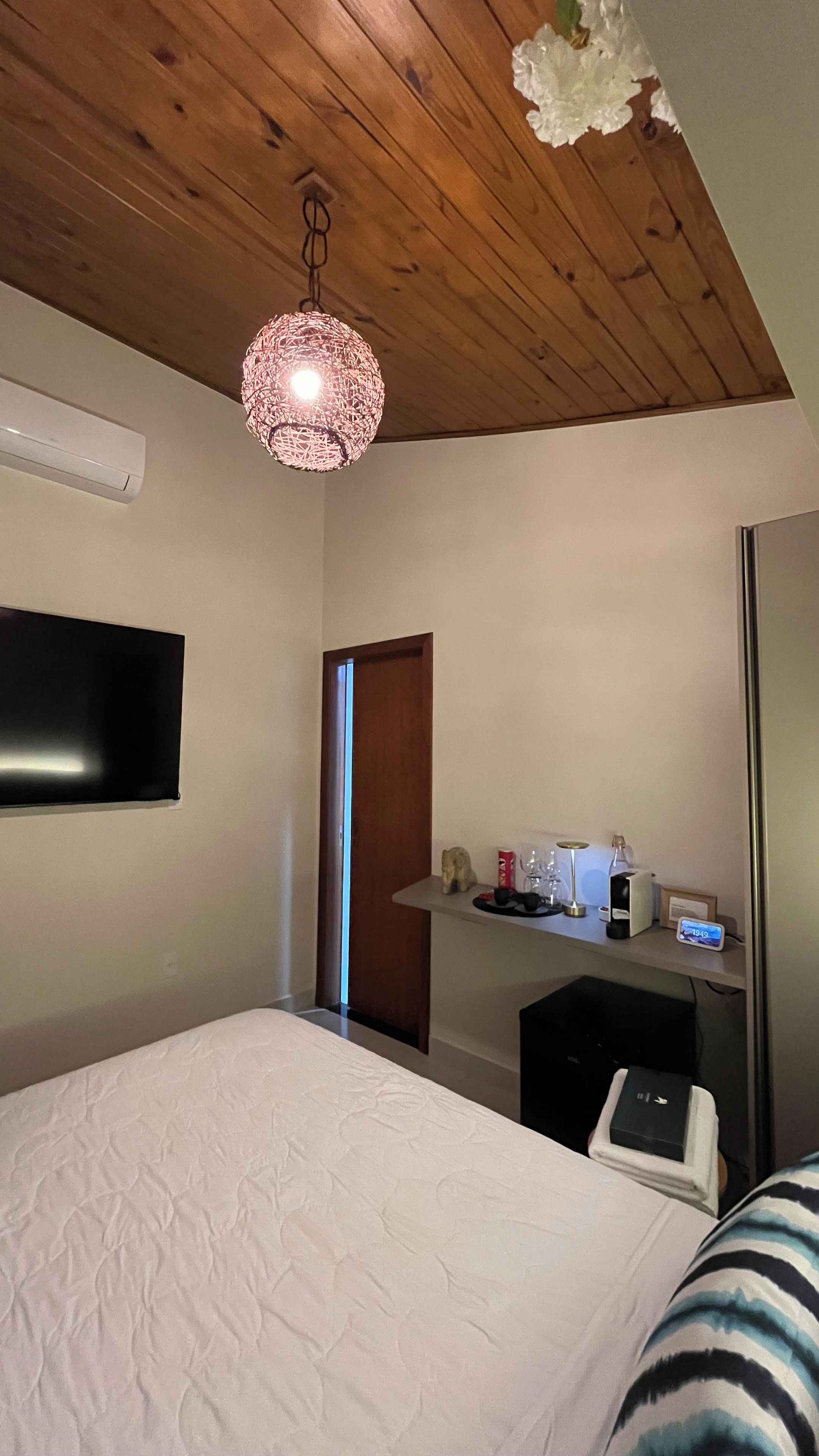 Une chambre d’hôtel comprenant un lit, une télévision, un bureau avec un ordinateur, une lampe décorative suspendue et une porte.