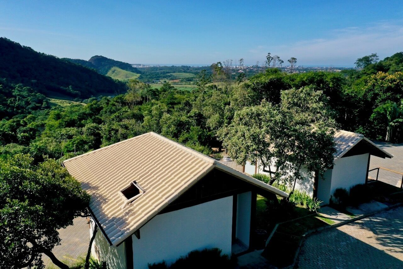 A view of a rural landscape with a white building with a sloped roof, surrounded by greenery and hills.