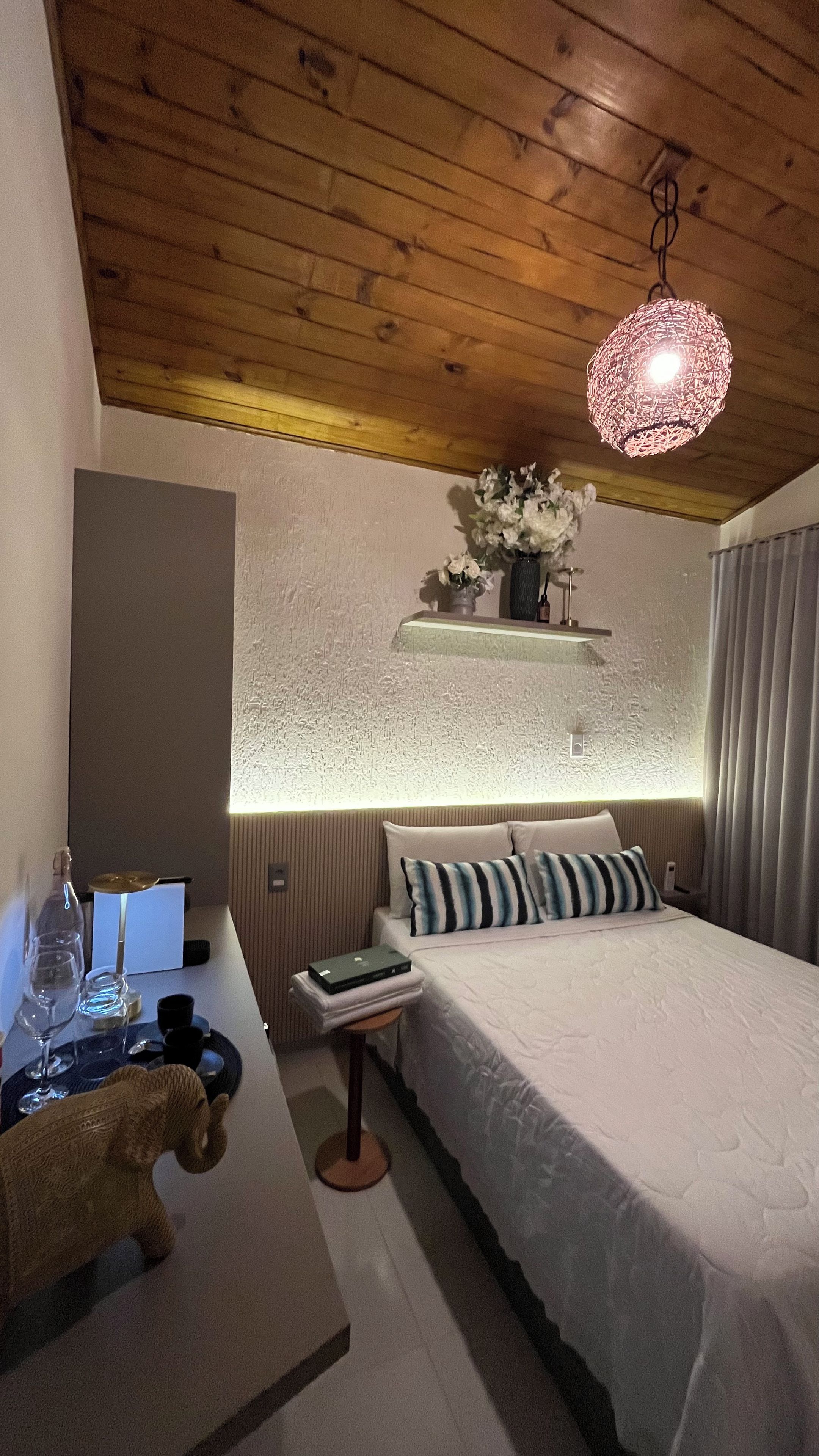 A bedroom with a bed, bedside table, lamp, and a hanging light fixture.