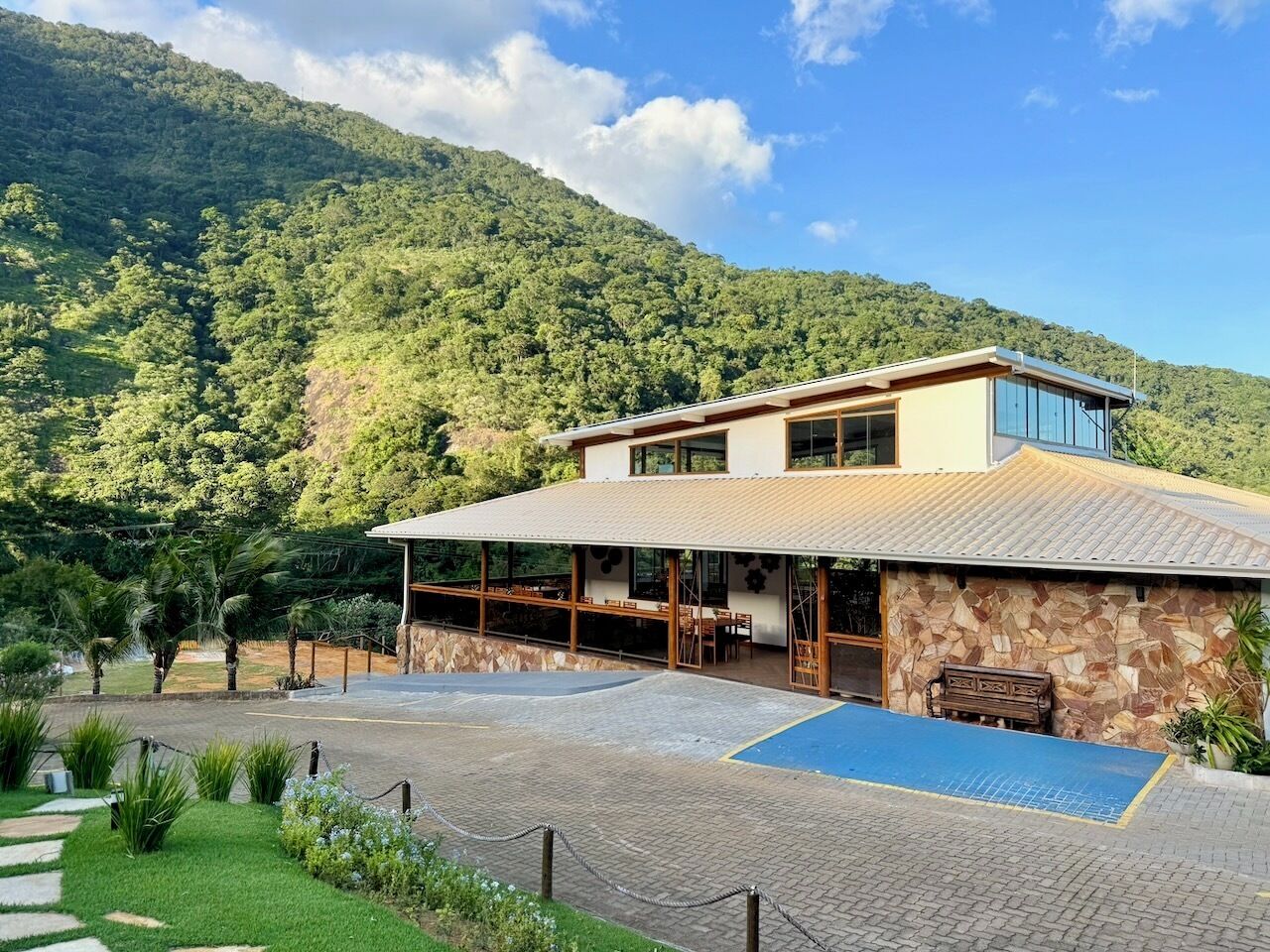 Un edificio moderno con un amplio patio, rodeado de exuberante vegetación y montañas al fondo.