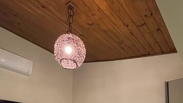 Un dormitorio con cama, mesita de noche, televisor, aire acondicionado instalado en la pared, techo de madera y lámpara colgante.