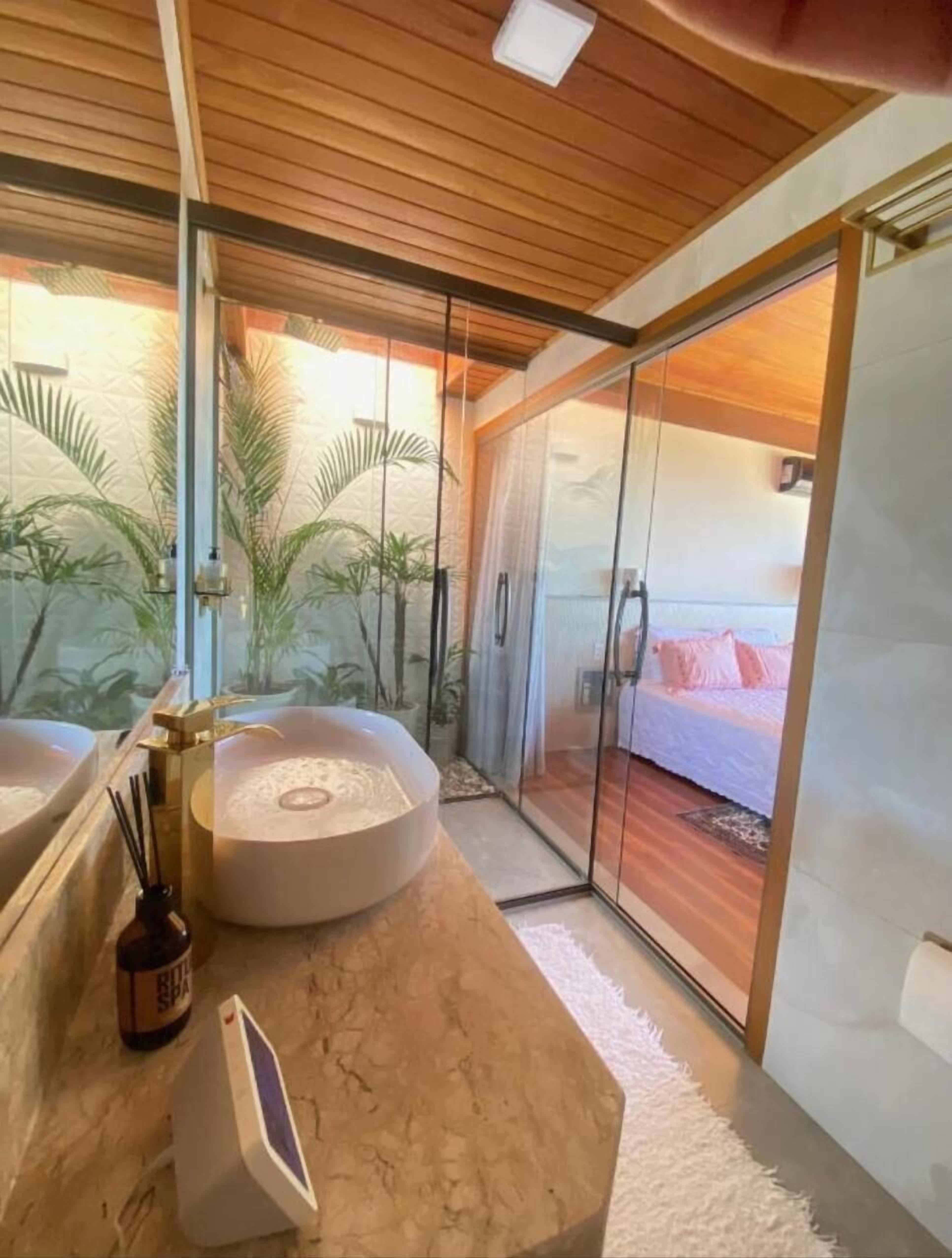 A modern bathroom with a large bathtub, a glass shower enclosure, and a view of a bedroom with a bed and curtains.