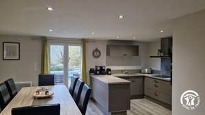 A modern kitchen with a dining area, a clock on the wall, and a view of the outdoors. - Peyre Blanque - LARROQUE (LARROQUE)