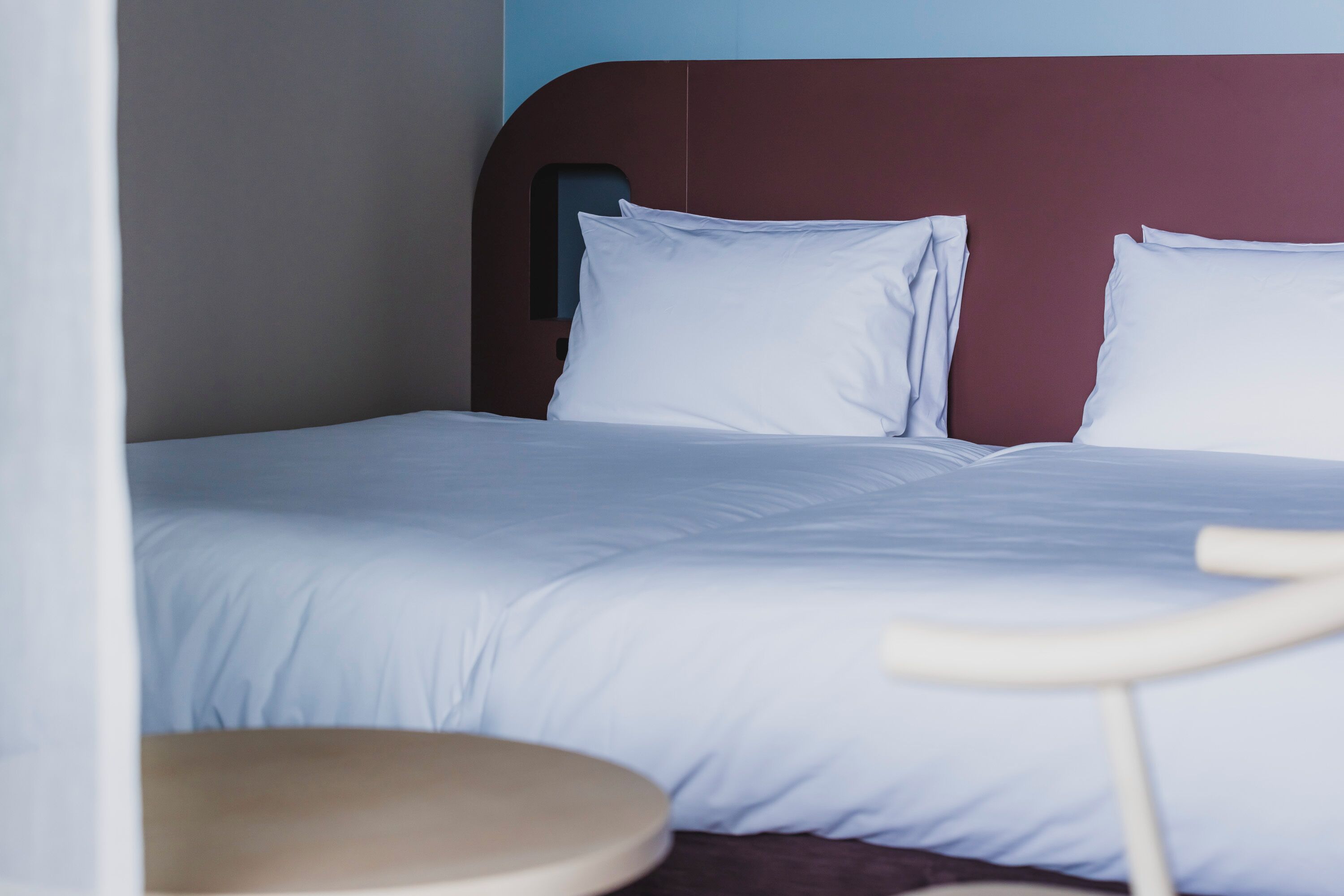 A bed with white bedding, a wooden headboard, and a round wooden chair.