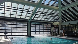 Una piscina interior con agua cristalina, rodeada de suelo de baldosas y un techo de vidrio.