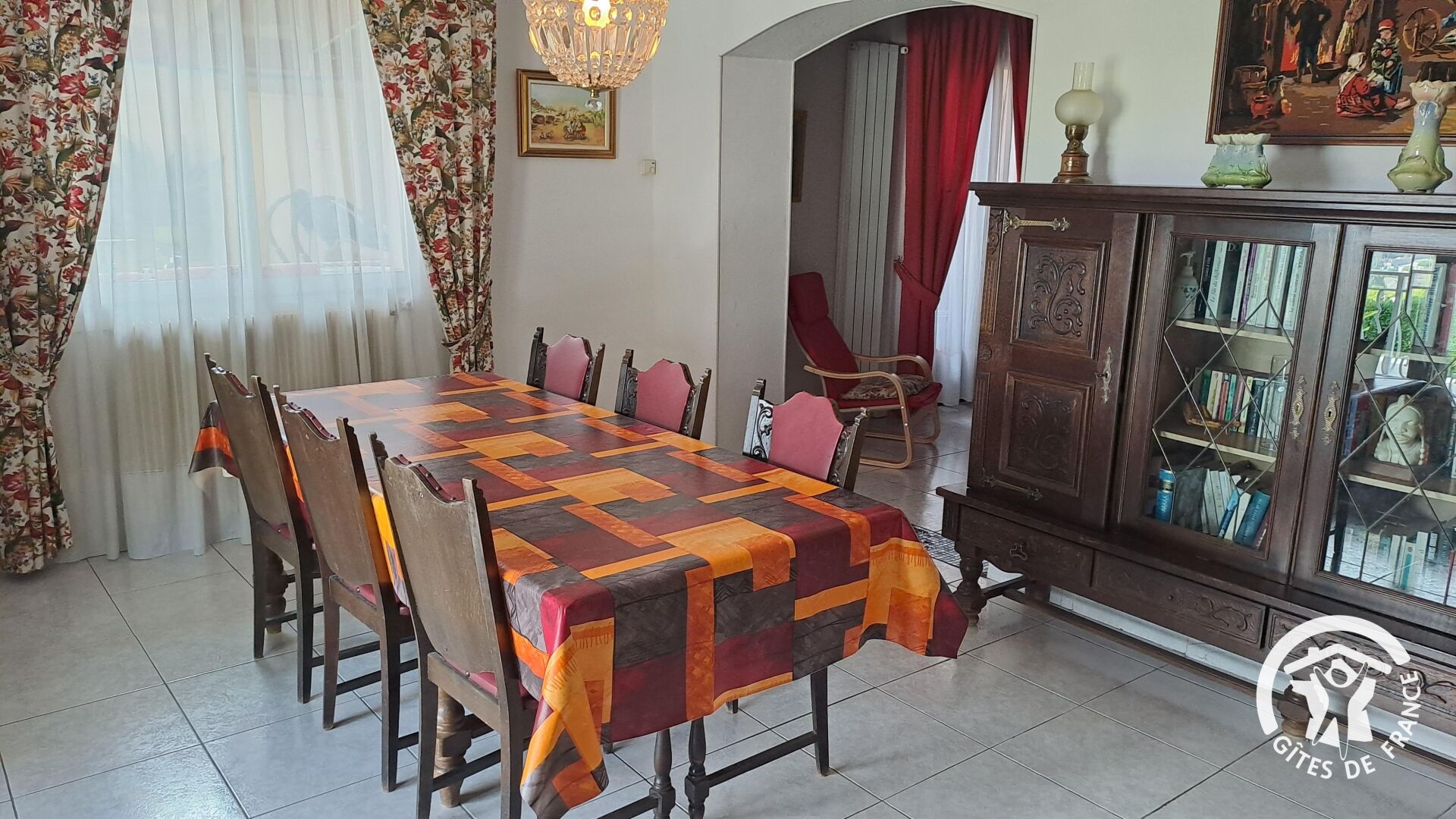 Un espace repas comprenant une longue table, des chaises, un meuble avec des livres et un lustre.