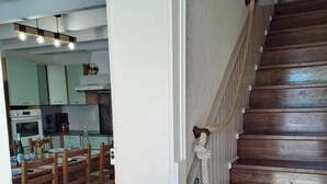 A wooden staircase with a white door leading to a dining area with wooden chairs and a kitchen in the background. - Le gîte du Vigneron - LABASTIDE-DE-LEVIS (LABASTIDE-DE-LEVIS)